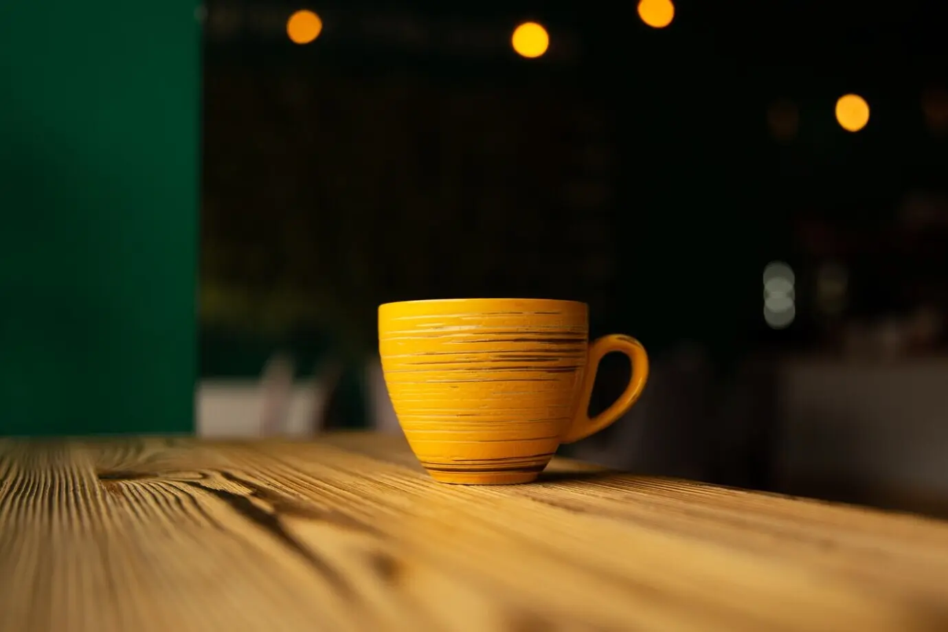 Leuchtend orangefarbene Tasse vor einem unscharfen dunklen Hintergrund mit Bokeh.